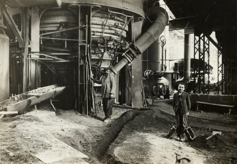 Homme et enfant devant un haut-fourneau